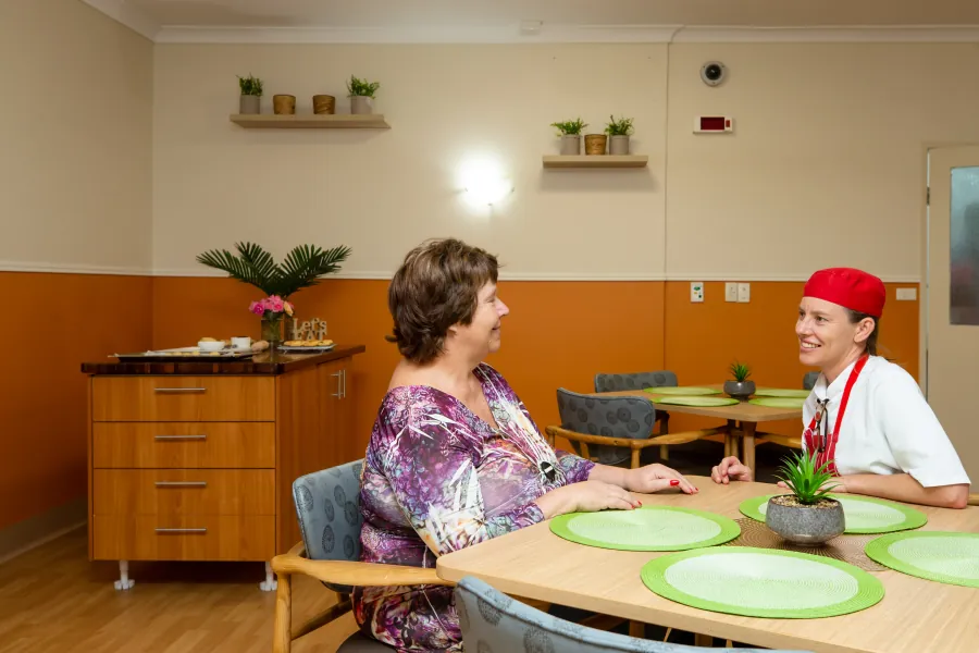 Two people talking at a dining-room table at Caloundra Place Care Community.