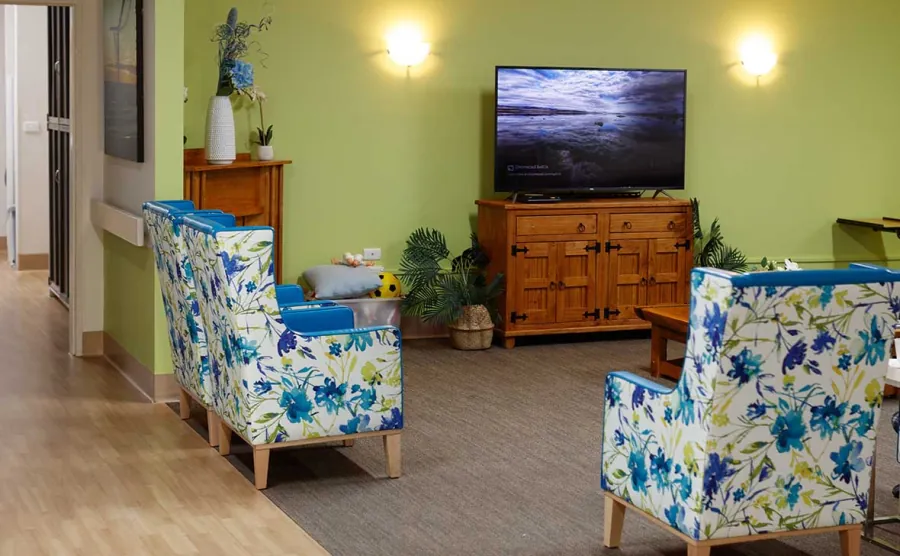 A lounge with floral armchairs and a television at Caloundra Place Care Community.